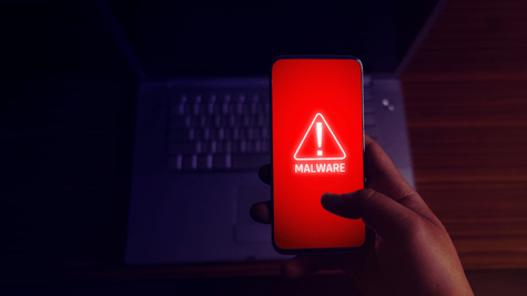 Hand holding mobile phone displaying malware warning with keyboard in background