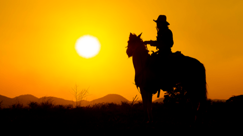Silhouetted wild west outlaw on horseback silhouetted against sunset