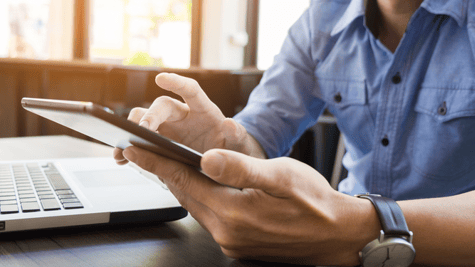 Hand holding mobile phone with laptop and work desk