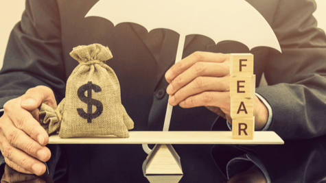 Businessman's torso with wooden scales balancing moneybag and word fear