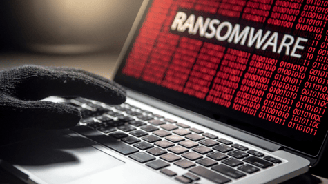 Hand with black glove typing on red matrix laptop screen with Ransomware inscription