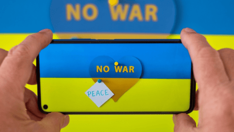 Mobile phone displaying Ukraine flag and antiwar message being held by male hands