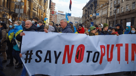 Crowd demonstrating in a city with a banner saying #SayNoToPutin