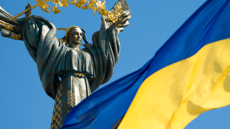 Ukrainian flag flying on sunny day with independence monument in background