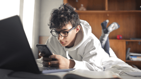 Teenage boy using mobile and laptop while lying on bed