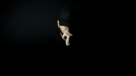 Young man in a black baseball cap, so deep in shadow you can only see part of his face.