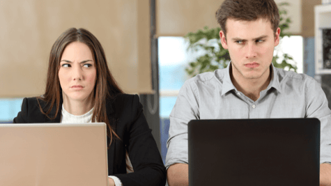 Two annoyed workers glaring at each over their laptops