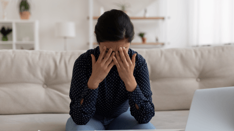 Woman holding head in hands after being scammed at home
