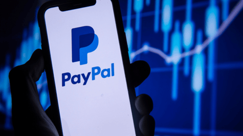 Shadowy hand clutching a mobile phone displaying the PayPal logo.