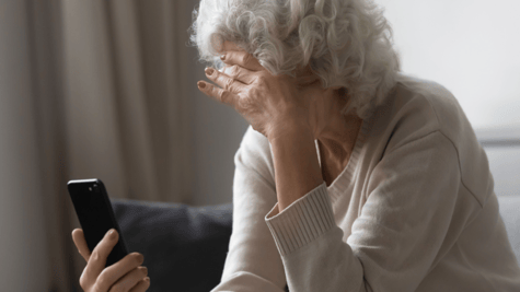 Elderly woman holds head in one hand and mobile in the other