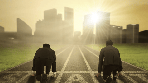 Two men in business dress kneeling on a race track towards a bright cityscape - but who wins?