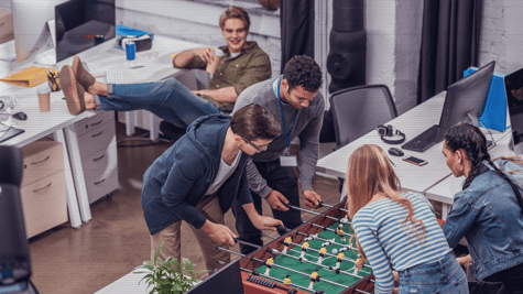 multiethnic colleagues playing in table soccer at modern office