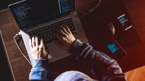 overhead hacker in the hood working with laptop and mobile phone typing text in dark room