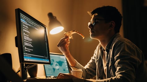 young programmer at home working and eating pizza