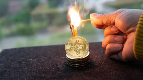 Hand holding lit matches to cryptocurrency coins