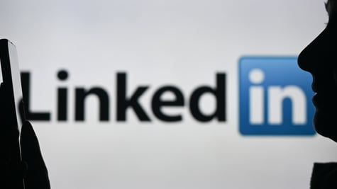 A person talking into their phone with the LinkedIn logo in the background.