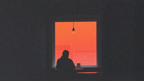 Remote work; the silhouette of a person sitting in front of a window, a shadow in a warm red light