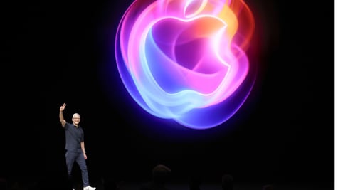 Apple CEO Tim Cook on black stage with two fingers up, glowing apple logo