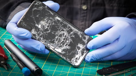 black smartphone with smashed screen held by hands in blue rubber gloves