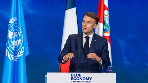 Emmanuel macron on podium with UN and France flag, blue background