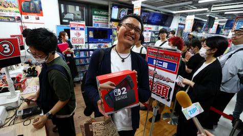 asian map smiling widely with eyes closed, holding nintendto switch 2 black box