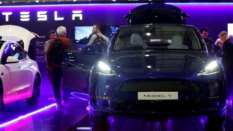 black tesla car on the right, open door on the left in a blue and purple lit room