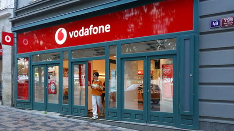 vodafone store with logo, asian woman walking out through the door in white throusers and orange top