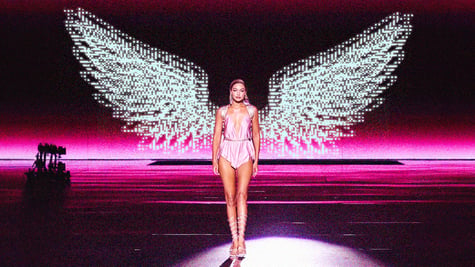 woman in shiny short pyjama on podium with digital angel wings