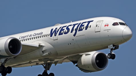 white plane in a blue sky, blue WestJet sign, canada flag