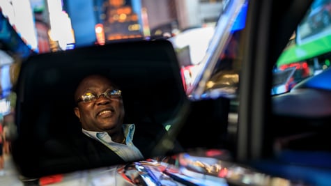 An uber driver, in the city, seeing himself in the wing-mirror.
