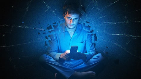 Someone scrolling their phone at night, with a broken background (could be glass).