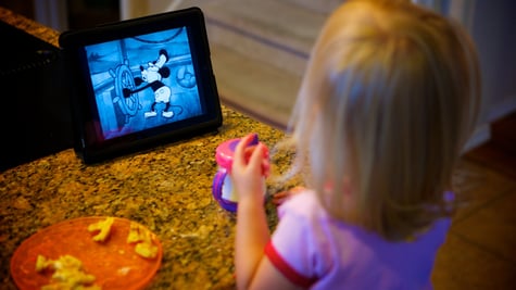 A small girl watching mickey mouse on her ipad.