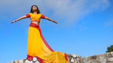 young indian woman standing on rock wall, yeallow red sari