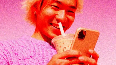 Alone young adult (Chinese) smiling at phone, milk tea nearby