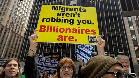 A person holding a sign that reads migrants aren't robbing you billionaires are