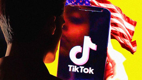 A person looks at a smartphone with a TikTok's logo on the screen, the US flag behind it