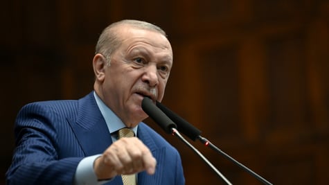 Recep Tayyip Erdogan in blue siot, baby blue shirt in front of two black vertical picrophones