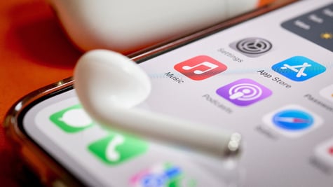 Airpod on top of iPhone screen displaying Apple Music app, Podcasts