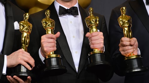 four golden oscars statues held in four mens hands in black suits