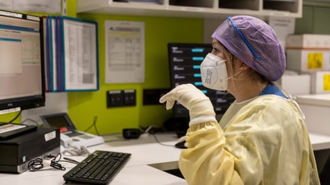 female nurse, blue har net, yellow scrub, computer monitor, white gloves, green wall