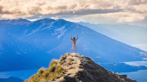 naked man on top of mountain, hands up, white clouds, grass, blue mountains, light blue sea