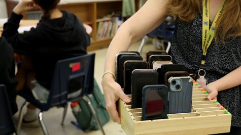 Teacher Heather Debby carries a box filled with students' cellphones in a classroom
