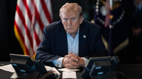 president donald trump sitsat desk, shadowy office, us flag in the back, blue shirt, no tis