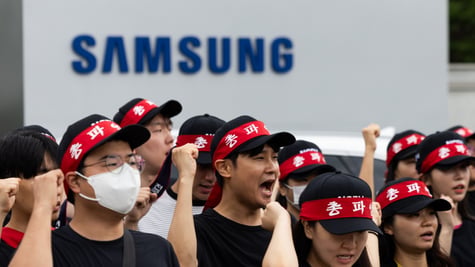 crowd of people with red bands around black hats chanting, samsung blue sign