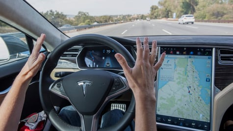 tesla black driving wheel, road ahead, two white hands not touching the wheel, map on screen