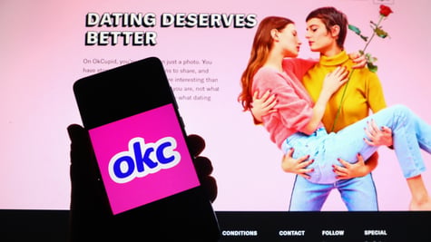 ok cupid logo, okc blue letters in white frame, pink bavkground, women kissing, red rose, screen