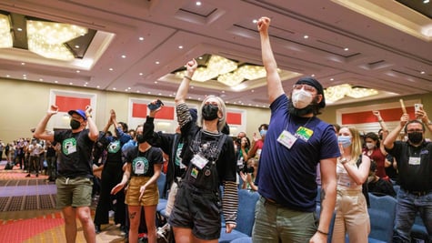 people with one hand up, white, black respirators, dark blue t-shirt, green shorts,  orange carpet 