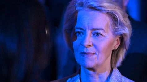 Ursula von der Leyen, blonde woman, semi-smile, white skin lit up in dark blue light 