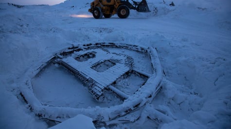bitcoin logo sculpture made from scrap metal, frozen on snow, mining truck in the background