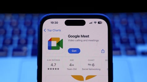 A laptop keyboard and Google Meet on App Store displayed on a phone screen